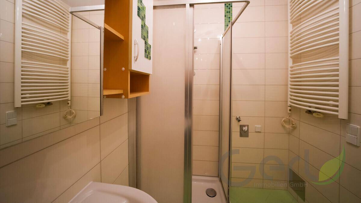 Helles Badezimmer mit Duschkabine, Fliesenboden und zwei Handtuchheizkörpern.