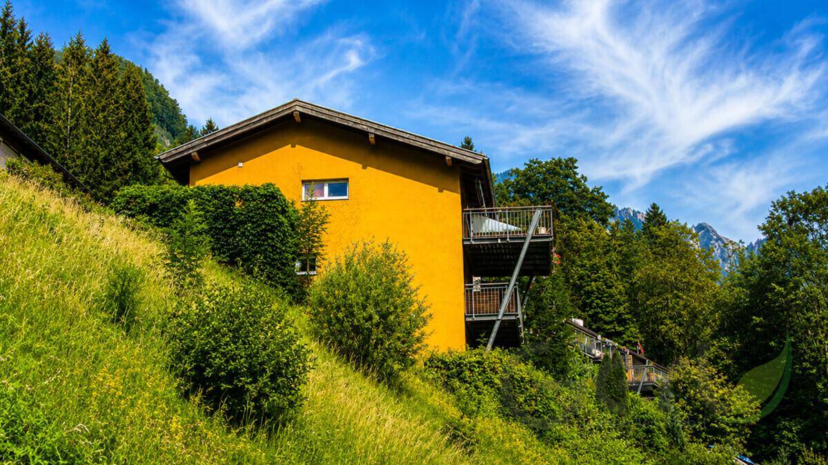 Gelbes Haus am Hang mit mehreren Balkonen und umgeben von üppiger Vegetation.