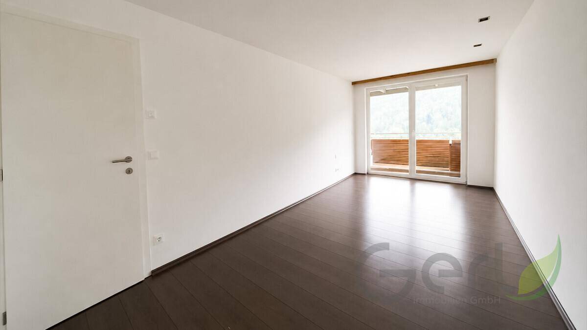 Helles, leeres Schlafzimmer mit dunklem Holzboden und Schiebetür zum Balkon.