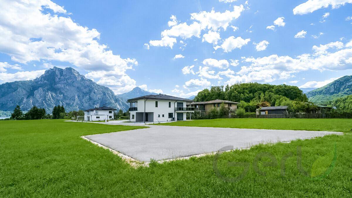 Weitläufige Grünfläche mit Neubauten und beeindruckendem Bergpanorama im Hintergrund.