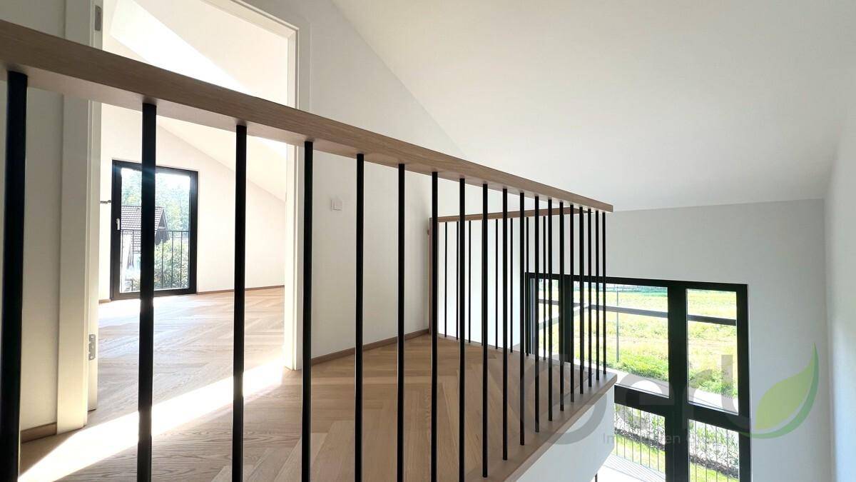 Heller Flur im Obergeschoss mit Holzgeländer und Blick ins Grüne durch große Fenster.