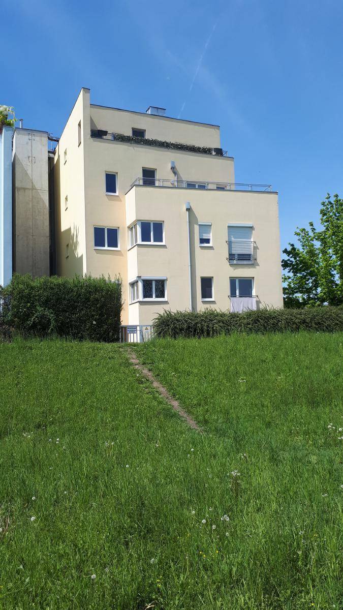 Ansicht eines modernen Wohngebäudes mit gelber Fassade und Terrassen, umgeben von einer grünen Wiese unter blauem Himmel.