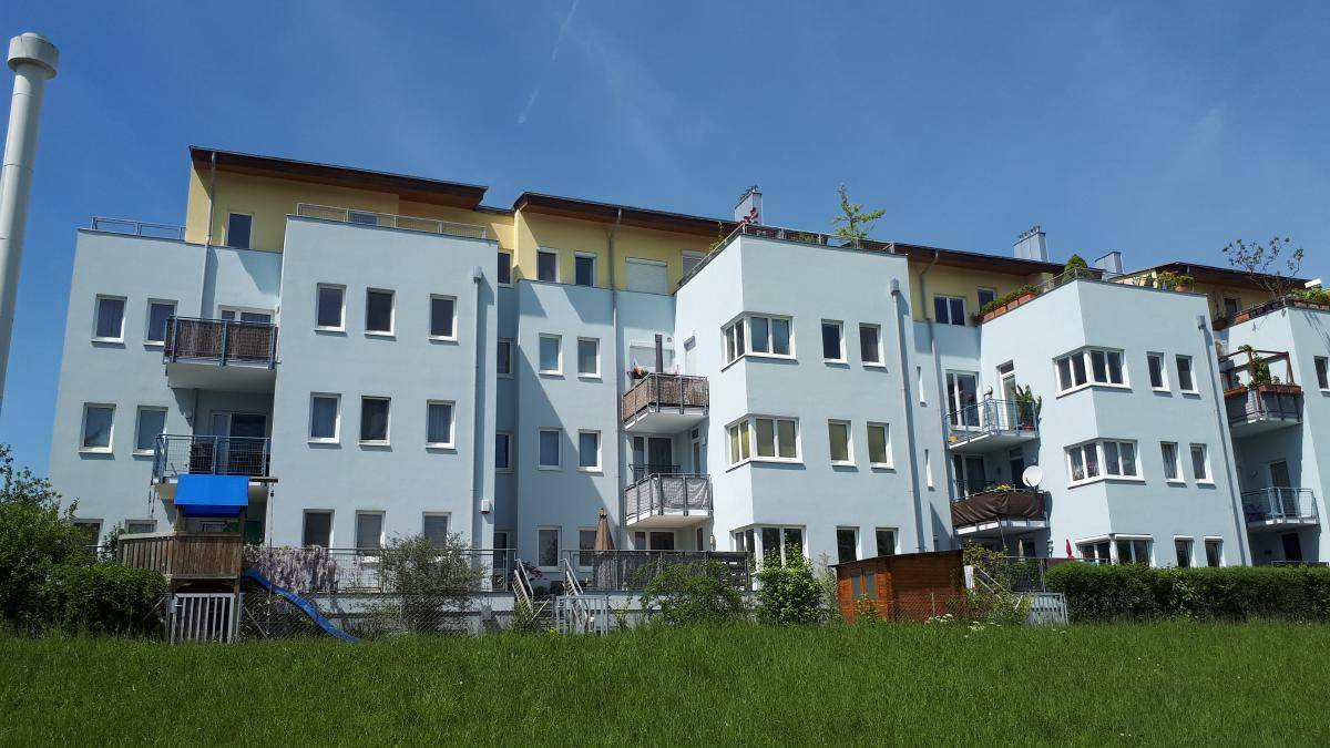 Moderne Wohnanlage mit hellblauen und gelben Fassaden, Balkonen und einem kleinen Spielbereich im Vordergrund.