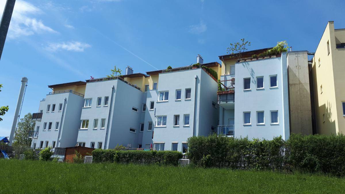 Ansicht einer modernen Wohnanlage mit gestuften Fassaden in Hellblau und Gelb, umgeben von einer gepflegten Grünfläche.