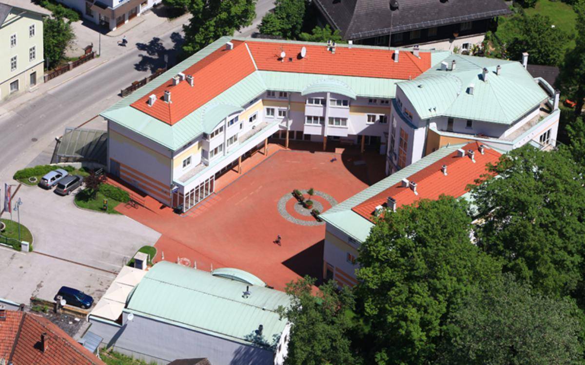 Luftaufnahme des Gebäudekomplexes mit rotem Dach und Innenhof, umgeben von Bäumen und Straßen.