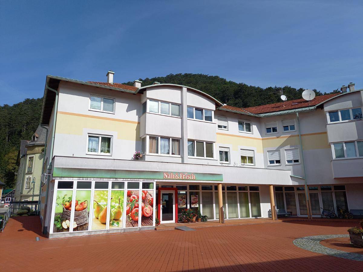 Gebäudefassade mit Ladenfronten im Erdgeschoss, darunter ein Geschäft mit 'Nah & Frisch' Beschriftung und Werbung.
