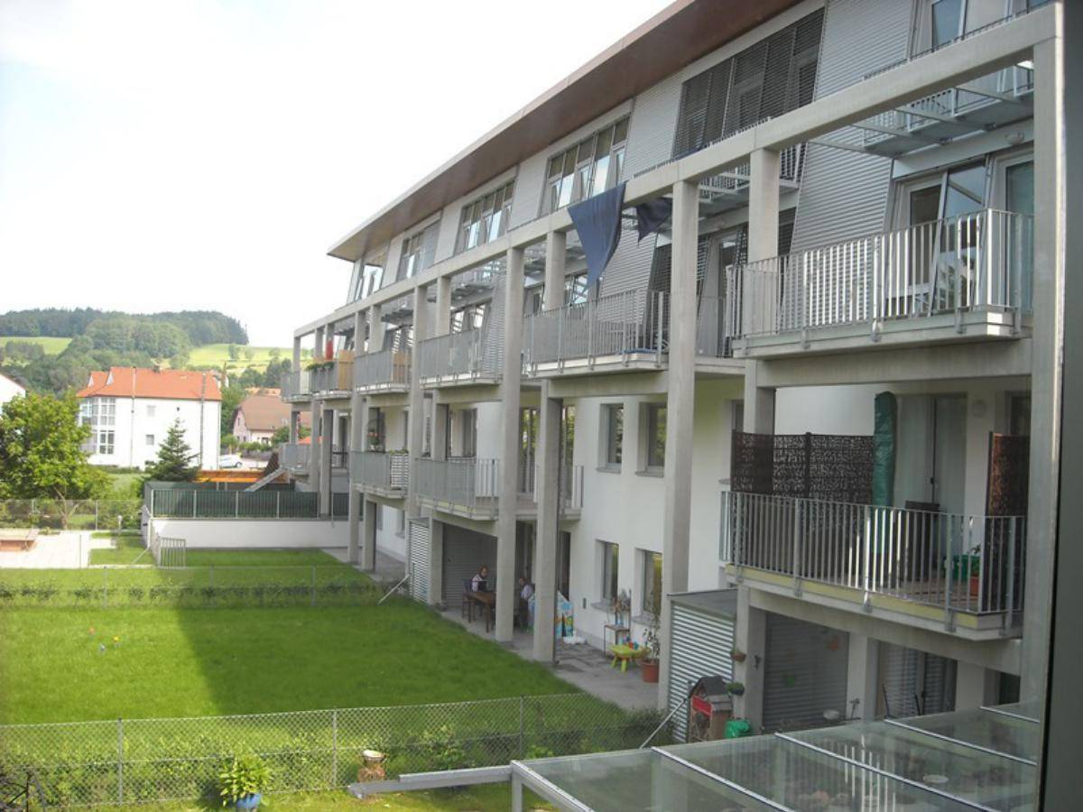 Seitenansicht des Gebäudes mit mehreren Balkonen, einer Rasenfläche und Blick auf die umliegende Landschaft.