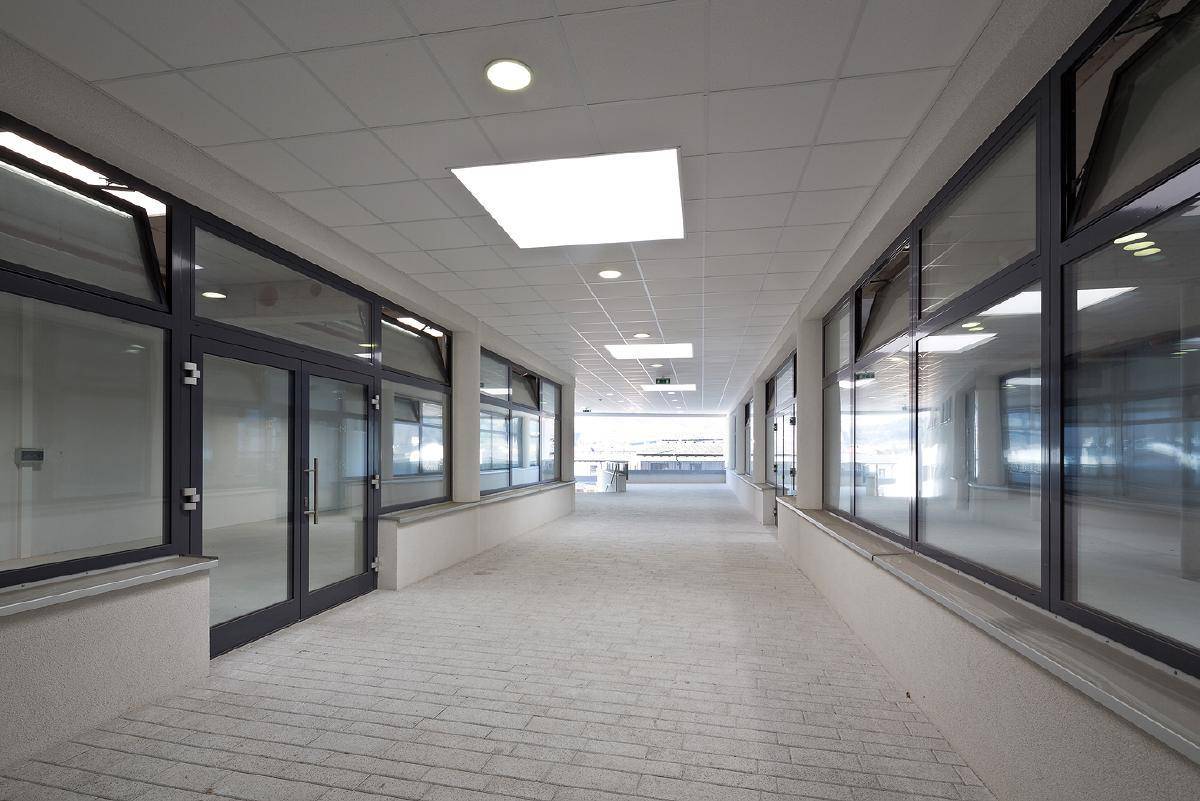Geräumiger, gut beleuchteter Gang mit großen Fensterfronten und moderner Deckenbeleuchtung.