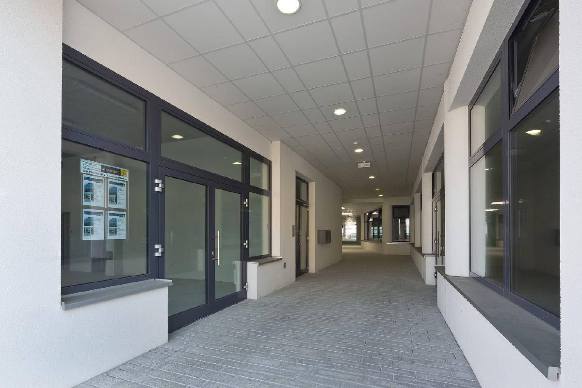 Langer, heller Flur mit großen Fenstern und abgehängter Decke in einem modernen Gebäude.