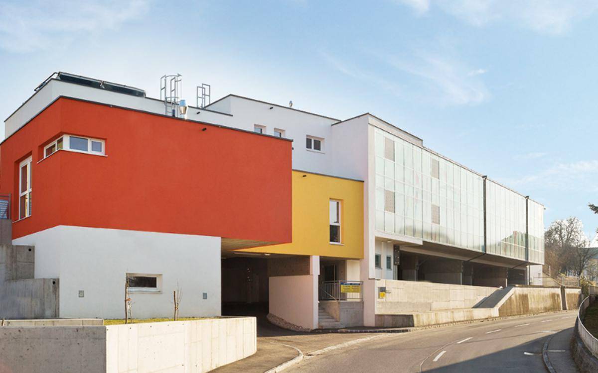 Architektonisch ansprechendes Gebäude mit farbigen Fassadenelementen in Orange und Gelb sowie einer Glasfassade.