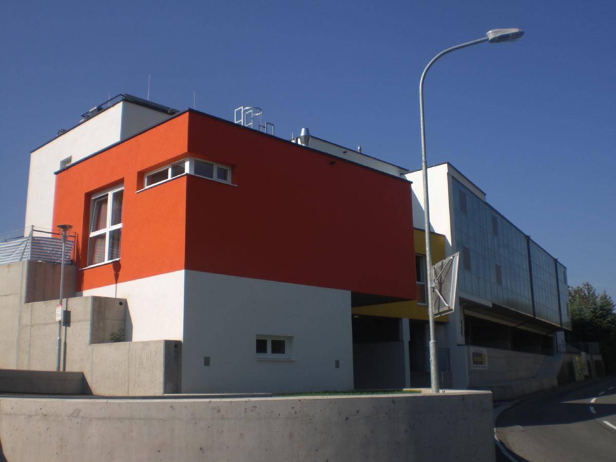 Moderne Architektur mit leuchtend orangefarbenen und gelben Akzenten an der Fassade, umgeben von Betonmauern.