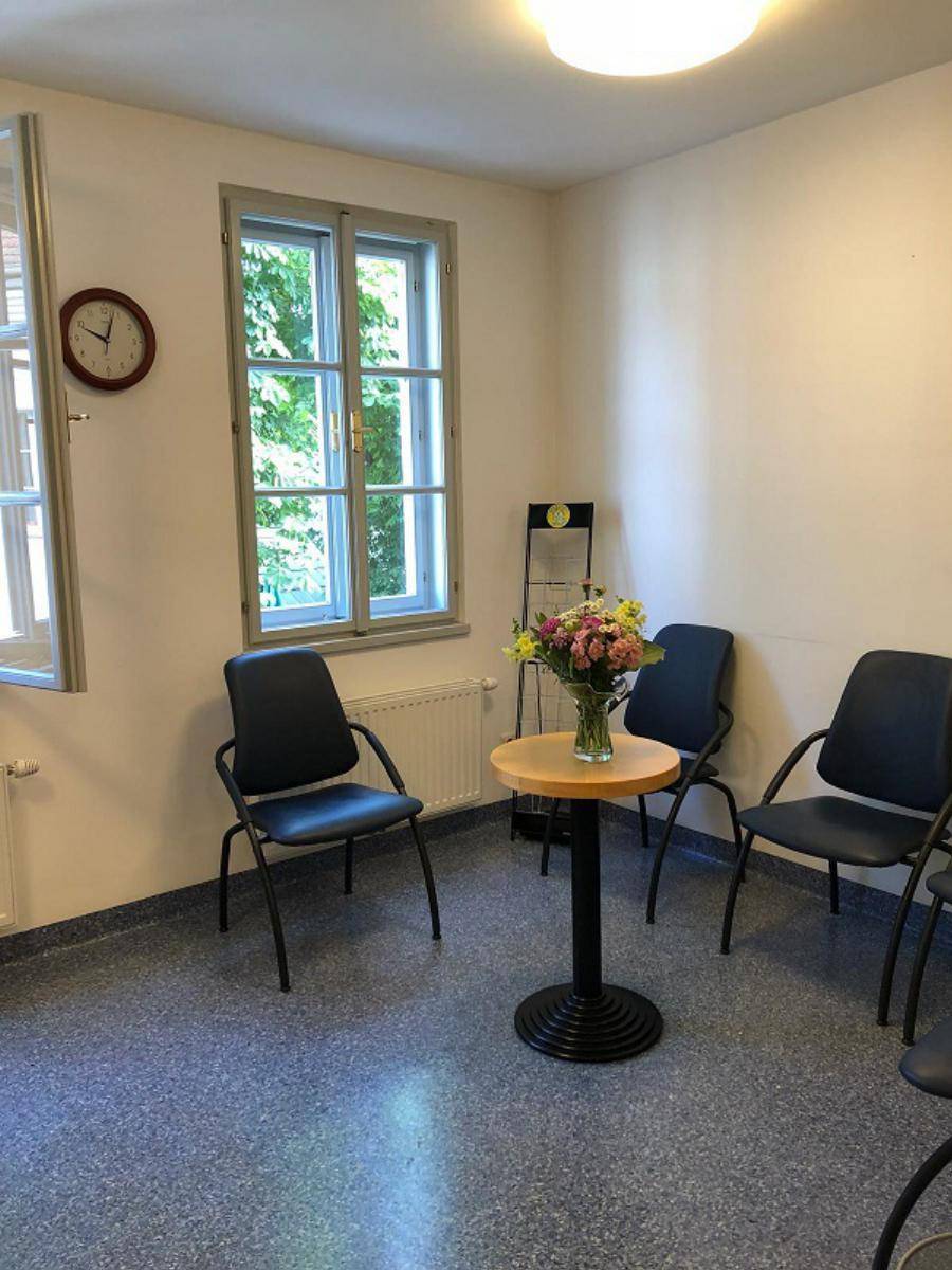 Wartezimmer mit mehreren Stühlen, kleinem Tisch und Fenster mit Blick ins Grüne.