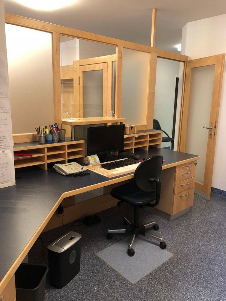 Empfangsbereich mit großem Schreibtisch, Computer und Bürostuhl, umgeben von Holz- und Glaselementen.