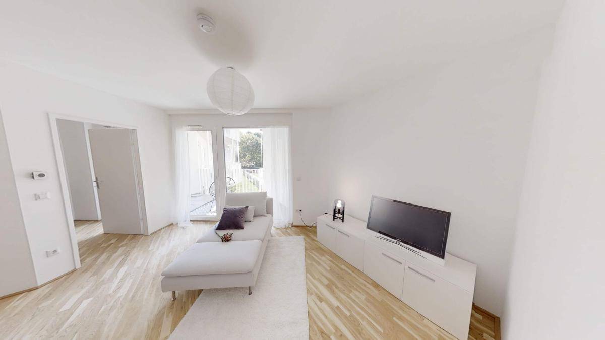Helles Wohnzimmer mit modernem Sofa, Fernseher und Zugang zum Balkon.