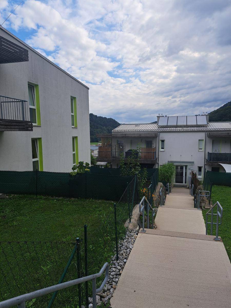 Blick auf die Rückseite des Wohnkomplexes mit Treppenweg, Rasen und Solaranlagen auf den Dächern.