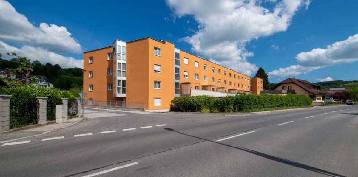 Ansicht des modernen Gebäudes mit orangefarbener Fassade an einer Straßenecke unter blauem Himmel.