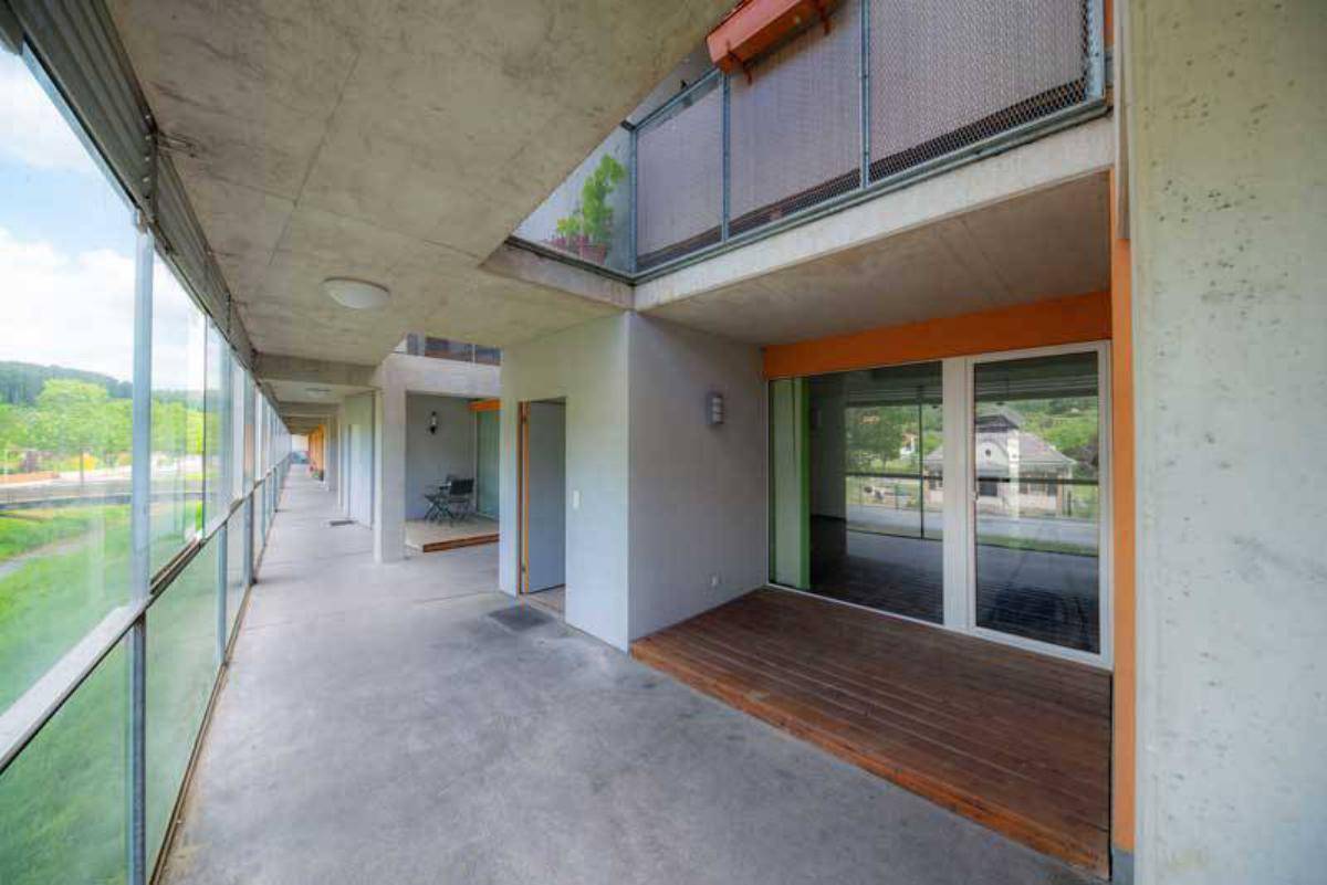 Langer, überdachter Balkon mit Holzboden und Zugang zu den einzelnen Wohneinheiten.