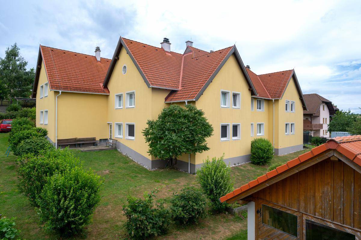 Ansicht des gelben Wohnhauses mit rotem Ziegeldach und gepflegtem Gartenbereich von der Seite.