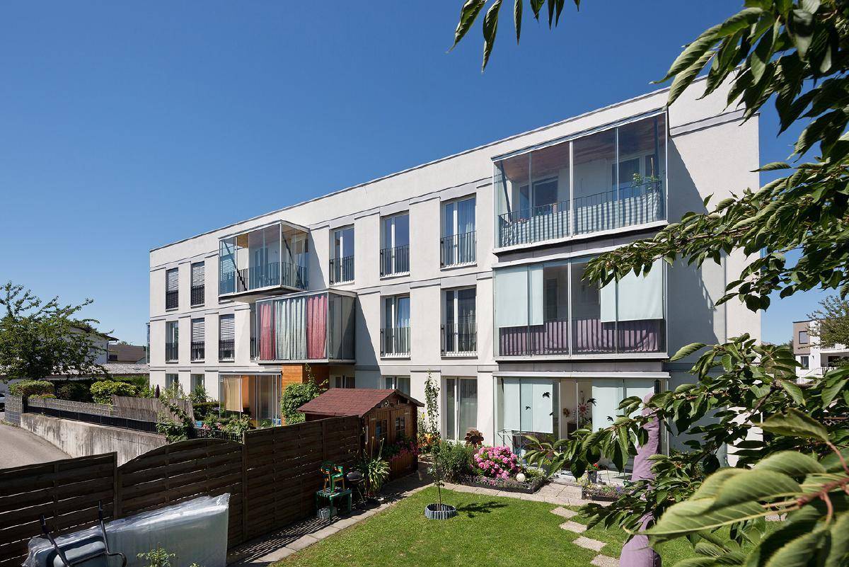 Rückseite der modernen Wohnanlage mit privaten Gärten, Gartenhäuschen und verglasten Balkonen.