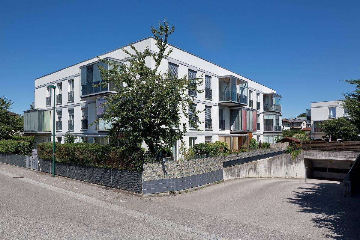 Ansicht der modernen Wohnanlage von der Straße mit Zufahrt zur Tiefgarage und umliegender Vegetation.