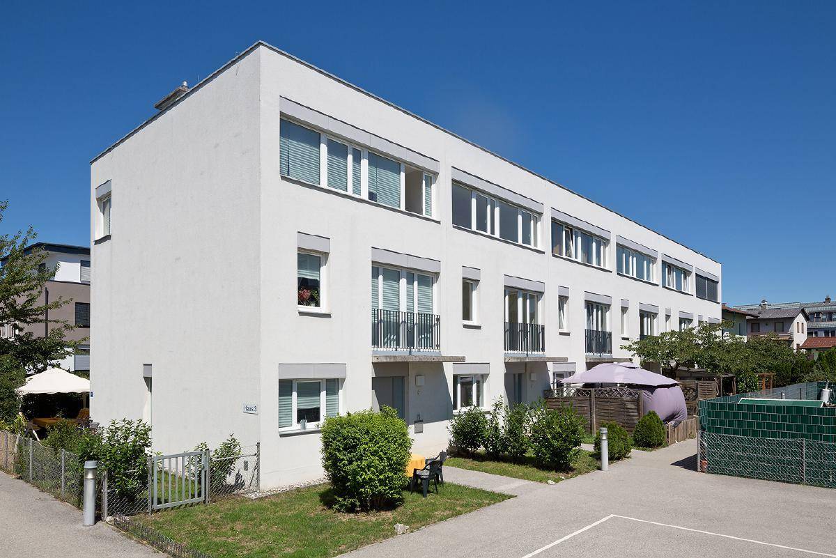 Reihenhausähnliche Wohngebäude mit kleinen Vorgärten und französischen Balkonen unter strahlend blauem Himmel.