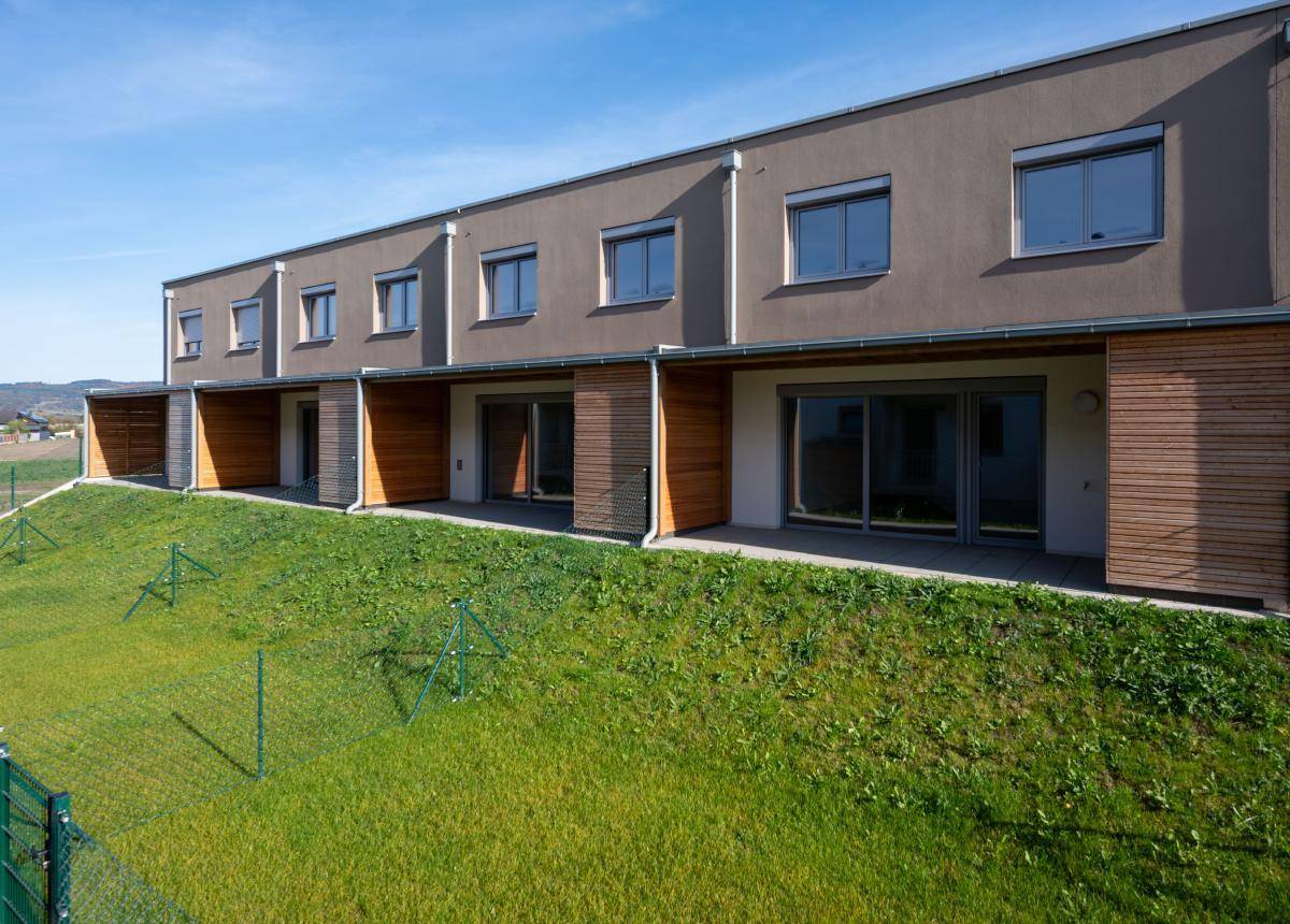 Rückseite moderner Reihenhäuser mit Terrassen und einer grünen Rasenfläche am Hang.