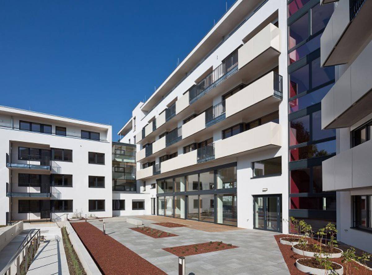 Heller Innenhof eines modernen Wohnkomplexes mit Balkonen und großen Glasfronten bei Sonnenschein.
