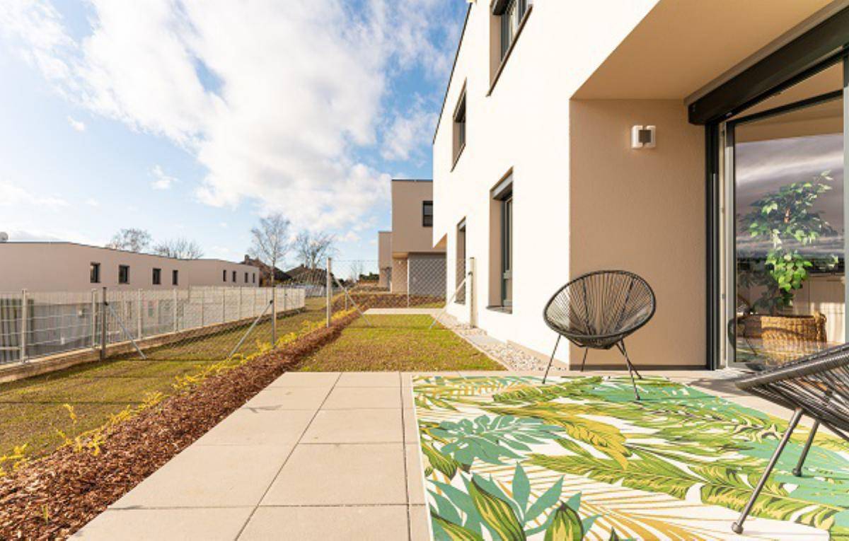 Sonniger Terrassenbereich mit modernen Fliesen, einem dekorativen Teppich und Blick ins Grüne.