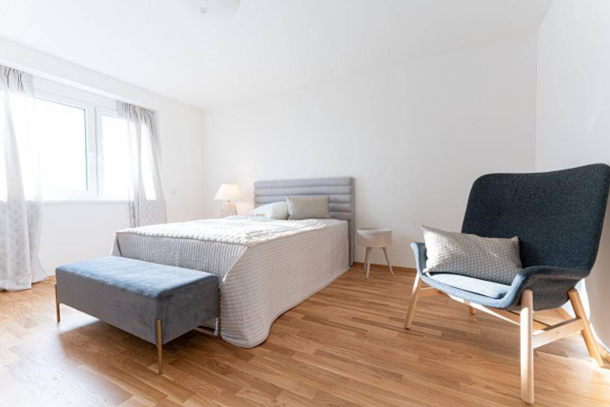 Helles Schlafzimmer mit Holzboden, modernem Bett und bequemen Sitzgelegenheiten am Fenster.