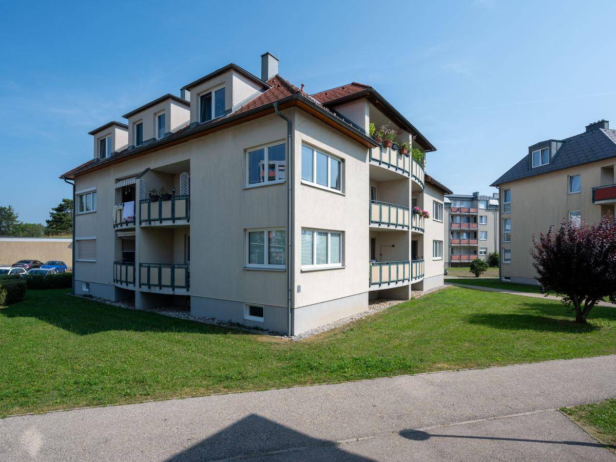 Mehrfamilienhaus mit hellen Fassaden, roten Ziegeldächern und Balkonen, umgeben von einer grünen Rasenfläche.