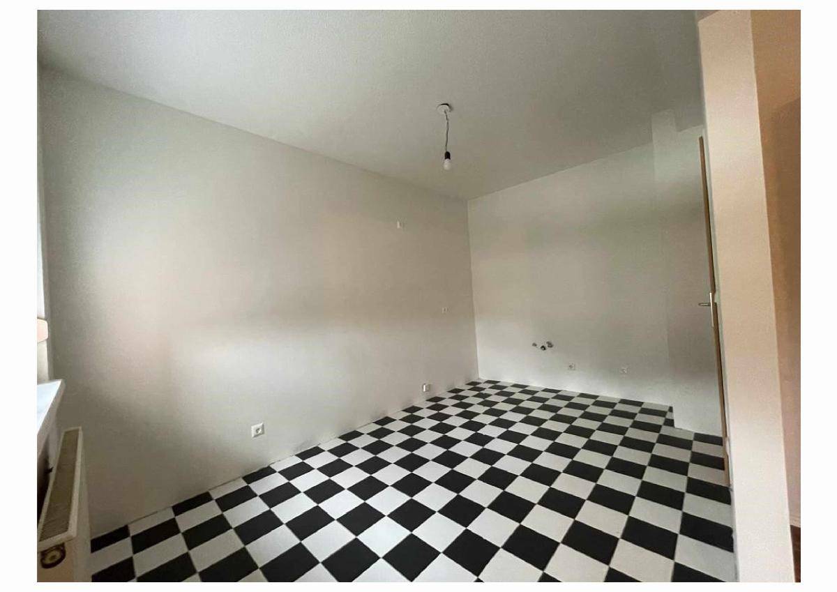 Leeres Zimmer mit markantem schwarz-weiß kariertem Fliesenboden und hellen Wänden.