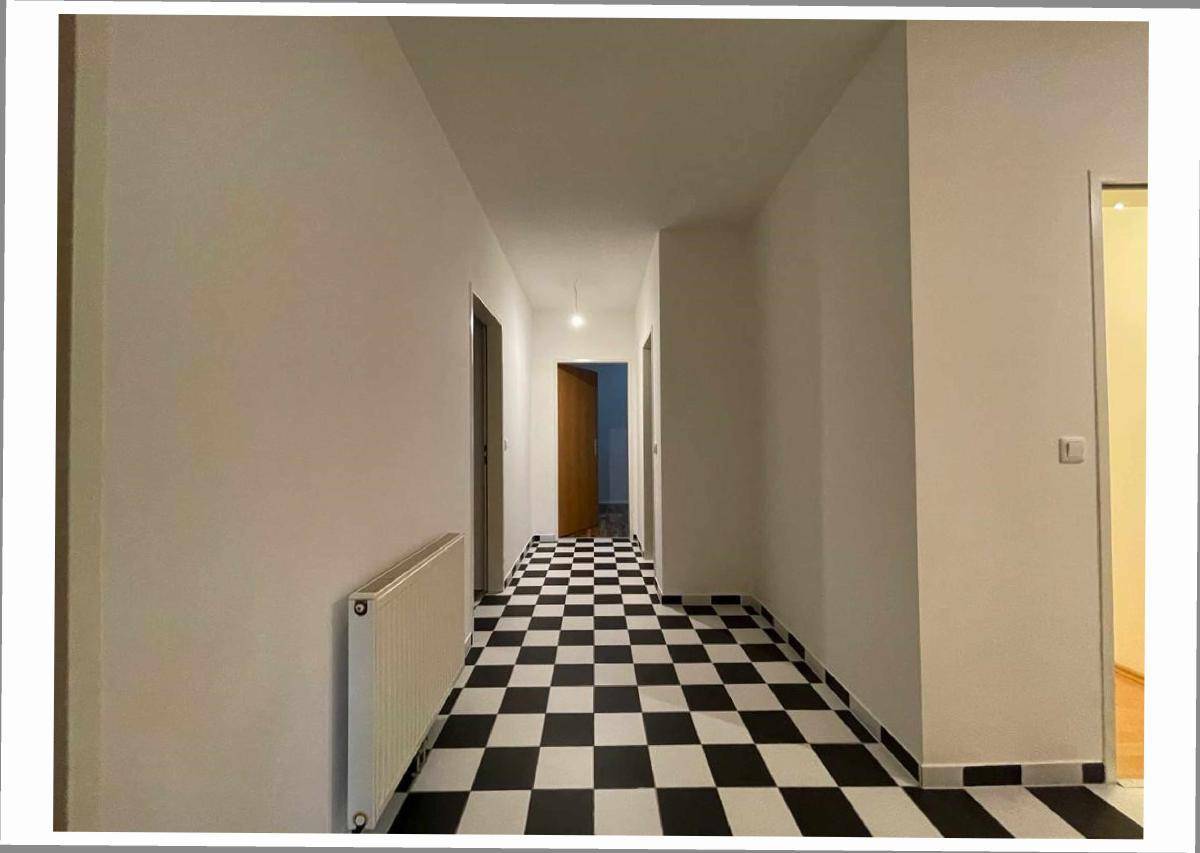 Langer Flur mit auffälligem schwarz-weiß kariertem Fliesenboden und Heizkörper.