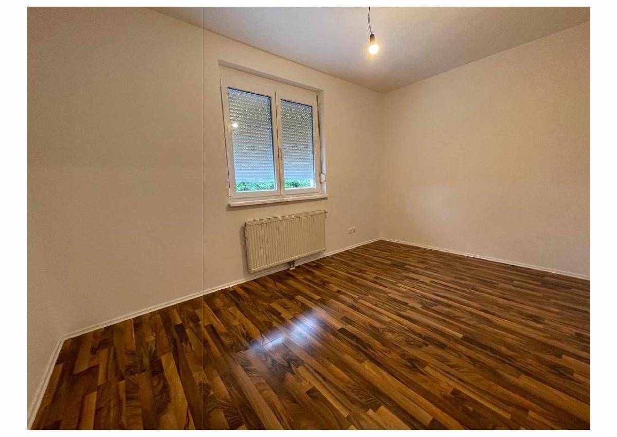 Helles Schlafzimmer mit Holzboden und einem Fenster, das viel Tageslicht hereinlässt.