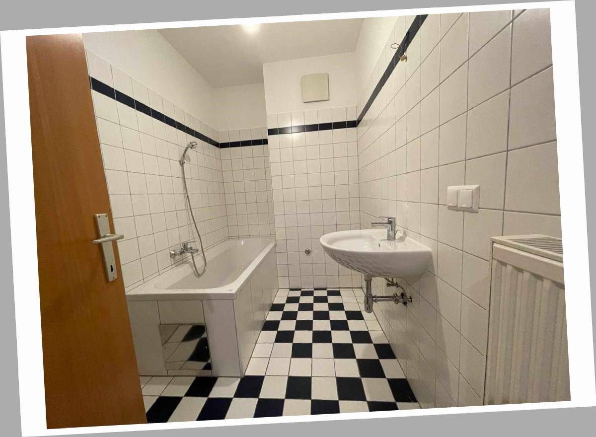 Badezimmer mit Badewanne, Waschbecken und schwarz-weiß kariertem Fliesenboden.