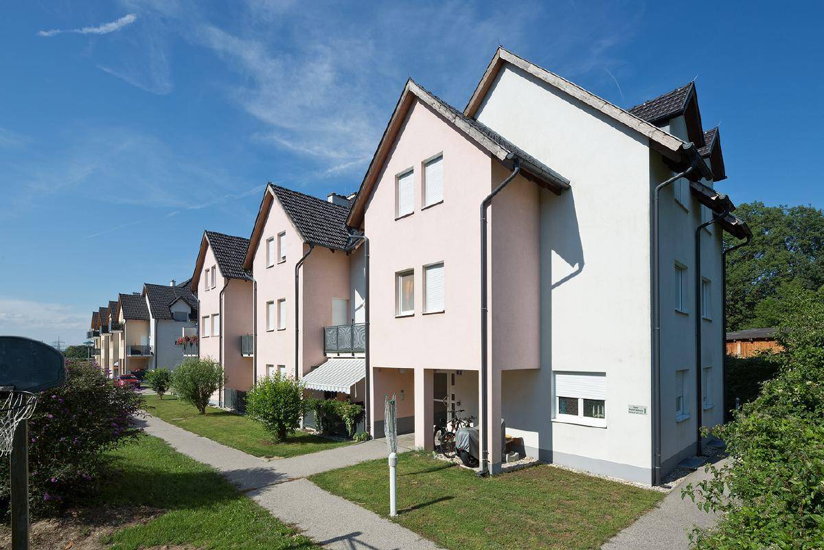 Seitenansicht einer Reihe von Wohnhäusern mit hellen Fassaden, Satteldächern und kleinen Balkonen in ländlicher Umgebung.