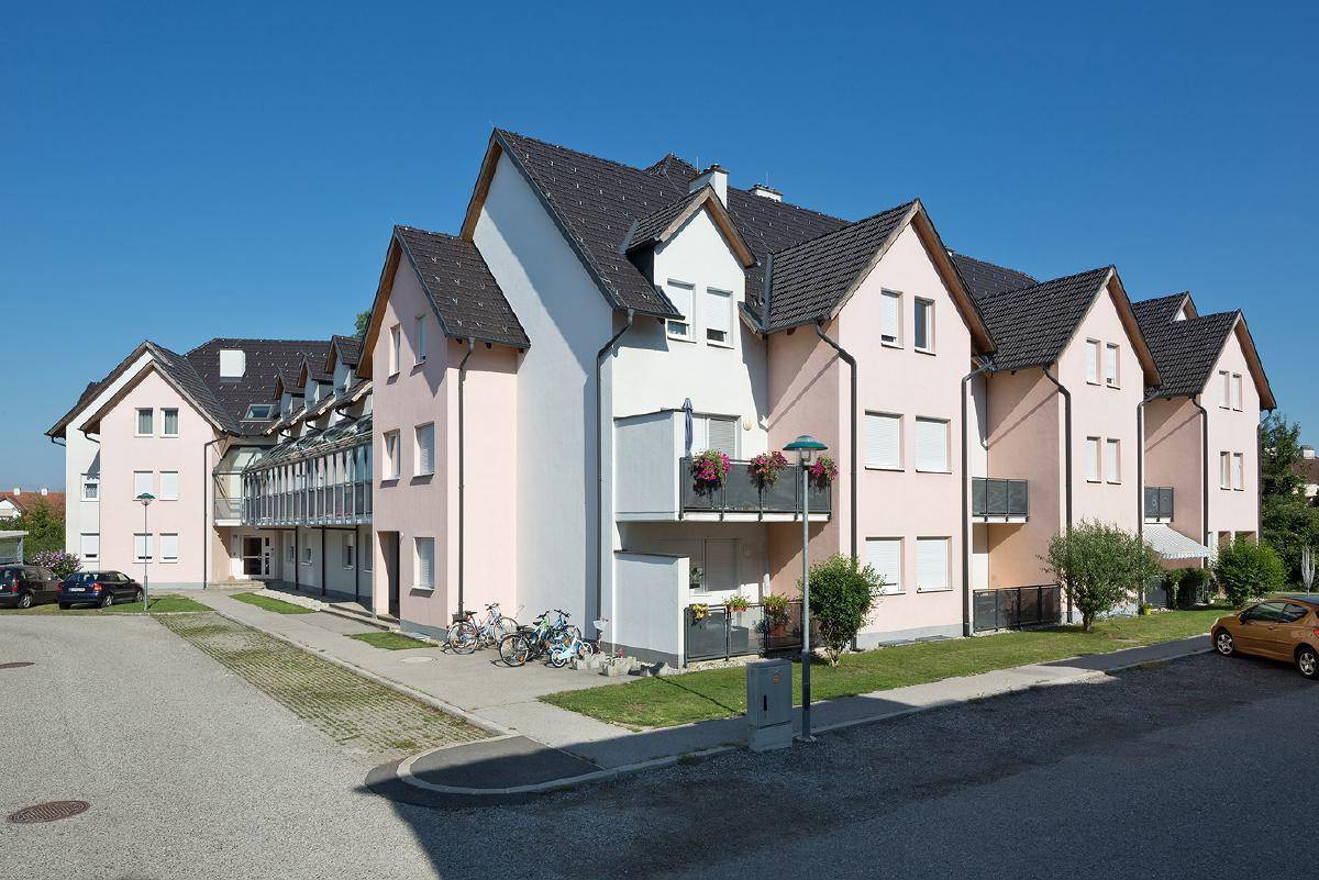 Gesamtansicht einer modernen Wohnanlage mit mehreren Gebäuden, Balkonen und Parkplätzen unter blauem Himmel.
