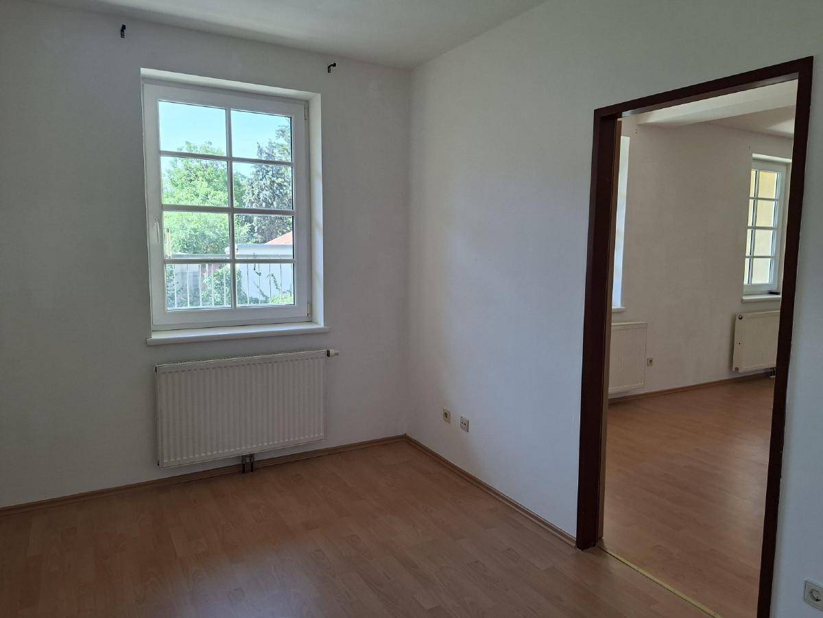 Leerer Raum mit Holzfußboden, großem Fenster und Blick ins Grüne.