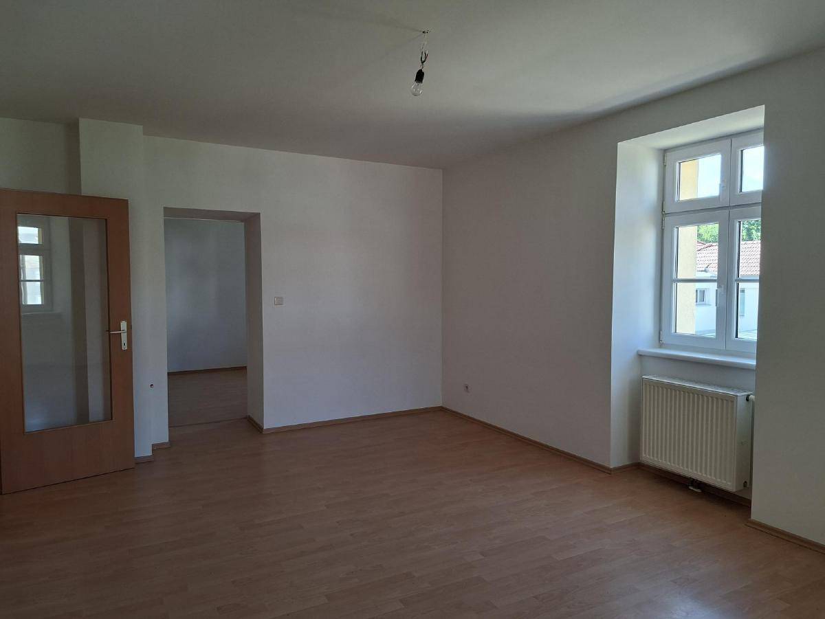 Heller, leerer Raum mit Laminatboden, weißen Wänden und Fenster.