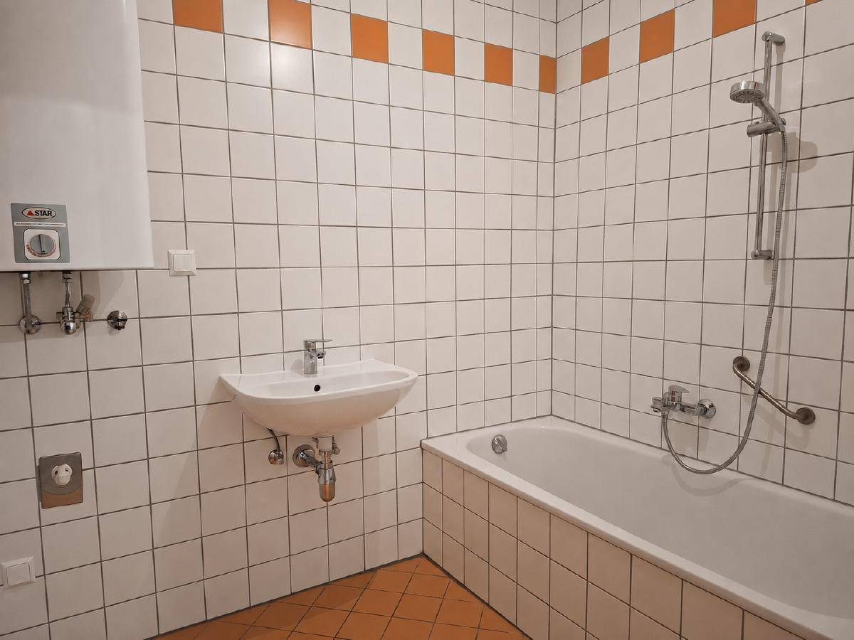 Badezimmer mit Badewanne, Waschbecken und weiß-orangen Fliesen.