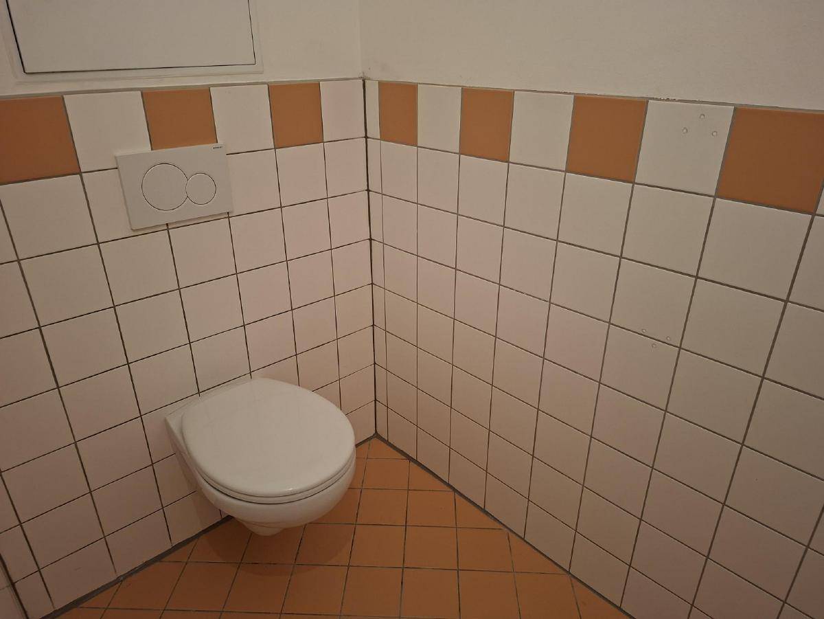 Separate Toilette mit Wand-WC und weiß-orangen Fliesen.