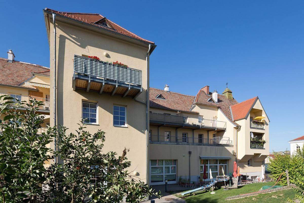 Seitenansicht des Gebäudes mit Balkonen und gepflegtem Gartenbereich.
