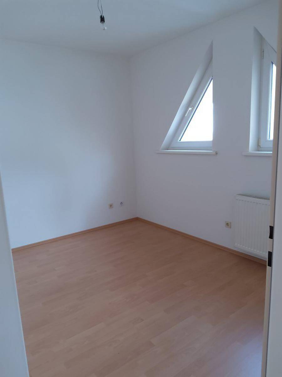 Leeres Zimmer mit Laminatboden und schrägem Dachfenster für viel Licht.