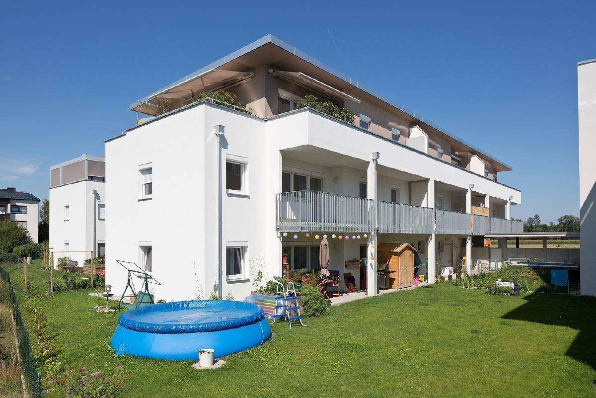 Modernes Wohngebäude mit Balkonen und einem Gartenbereich inklusive kleinem Planschbecken.