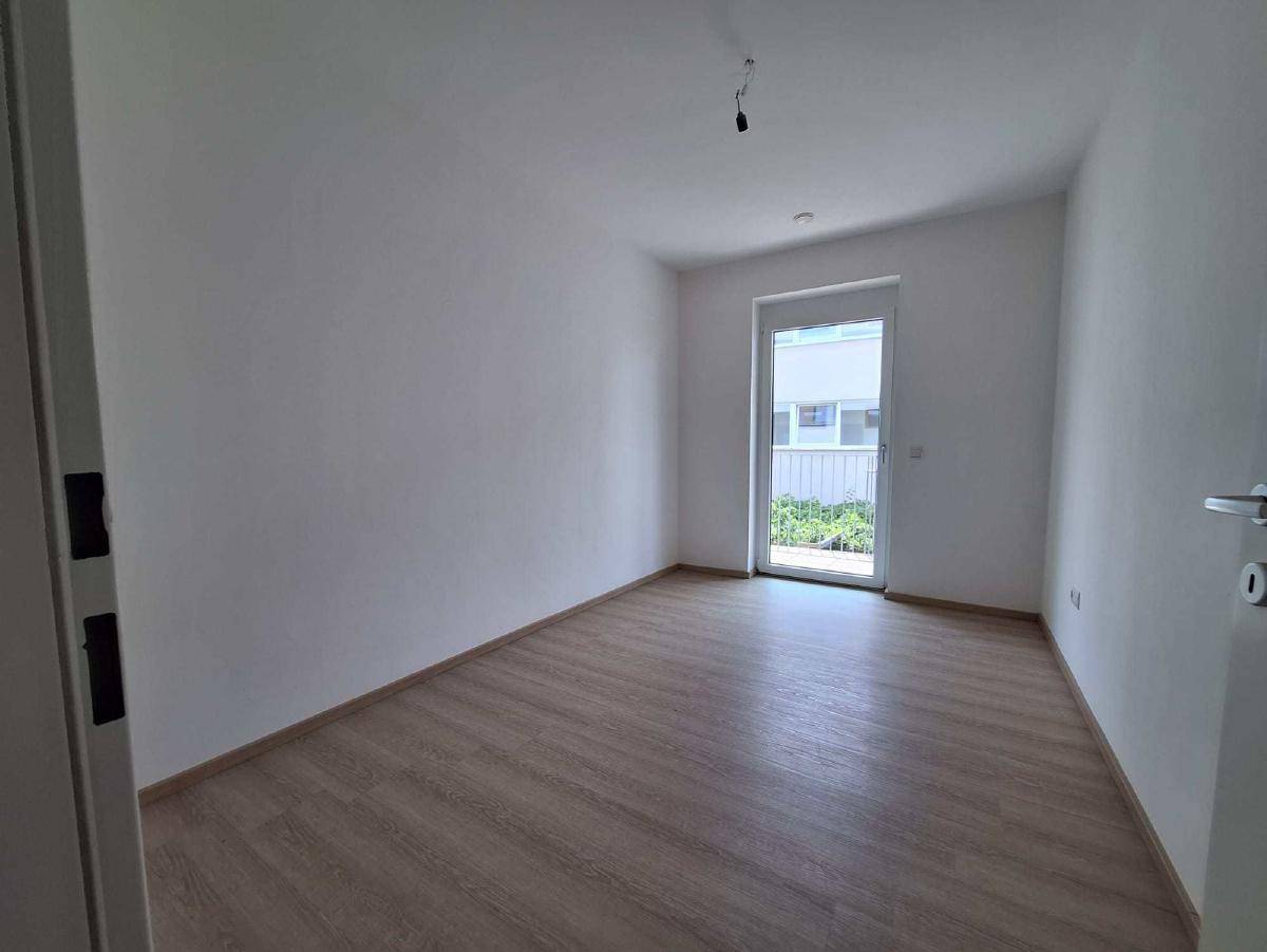 Helles, leeres Schlafzimmer mit Laminatboden und Zugang zu einem Balkon.