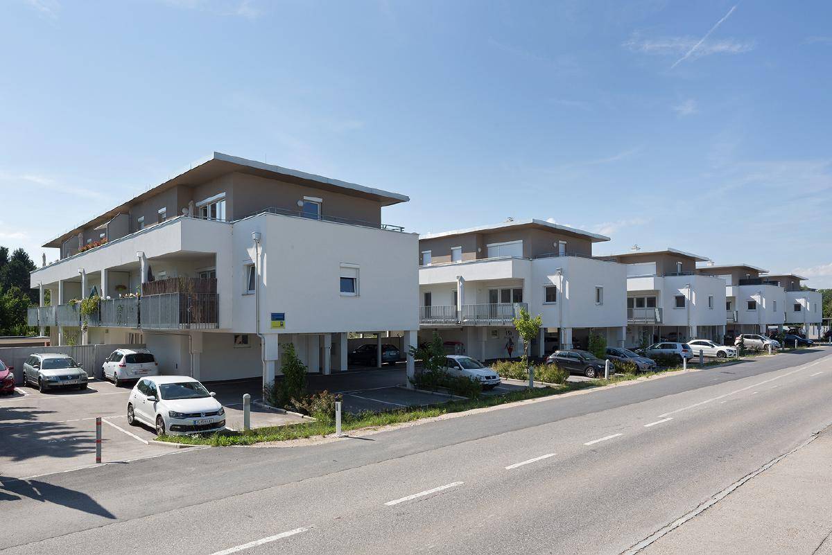Reihe moderner Mehrfamilienhäuser mit Parkplätzen entlang einer ruhigen Straße.