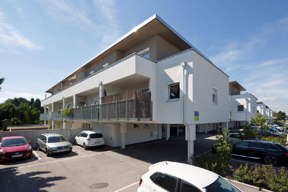 Modernes Mehrfamilienhaus mit weißer Fassade und zugehörigen Parkplätzen im Freien.