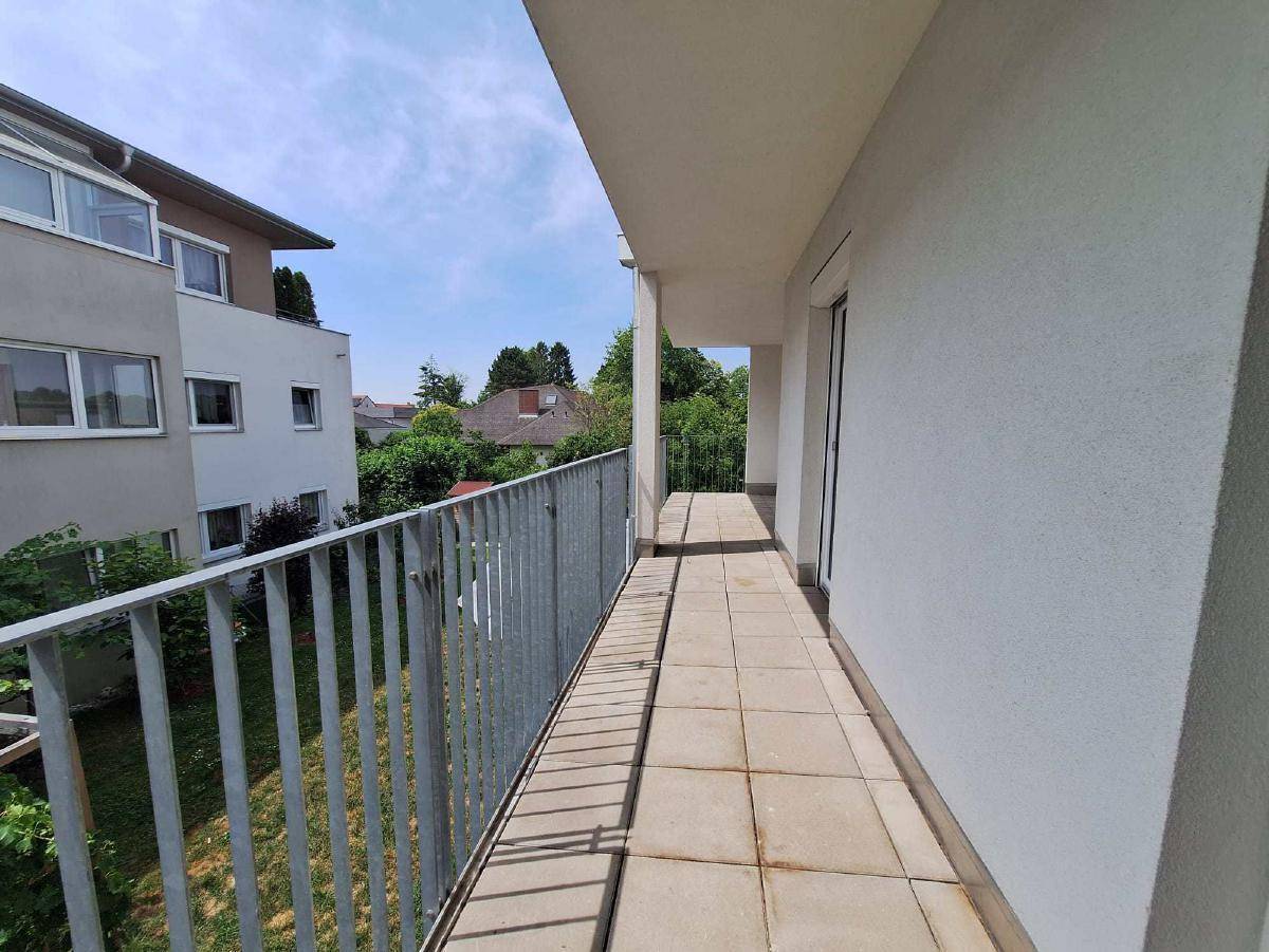Langer, schmaler Balkon mit Fliesenboden und Metallgeländer, bietet Blick ins Grüne.