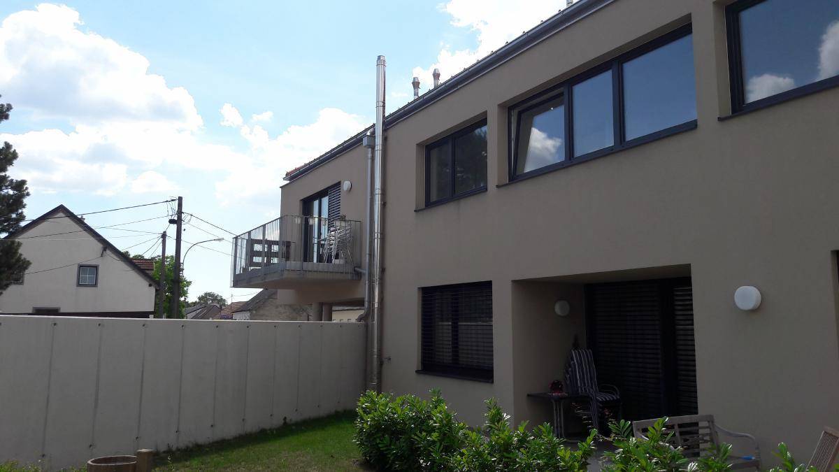 Rückseite des Gebäudes mit einem Balkon, einer kleinen Terrasse und einem umzäunten Gartenbereich.