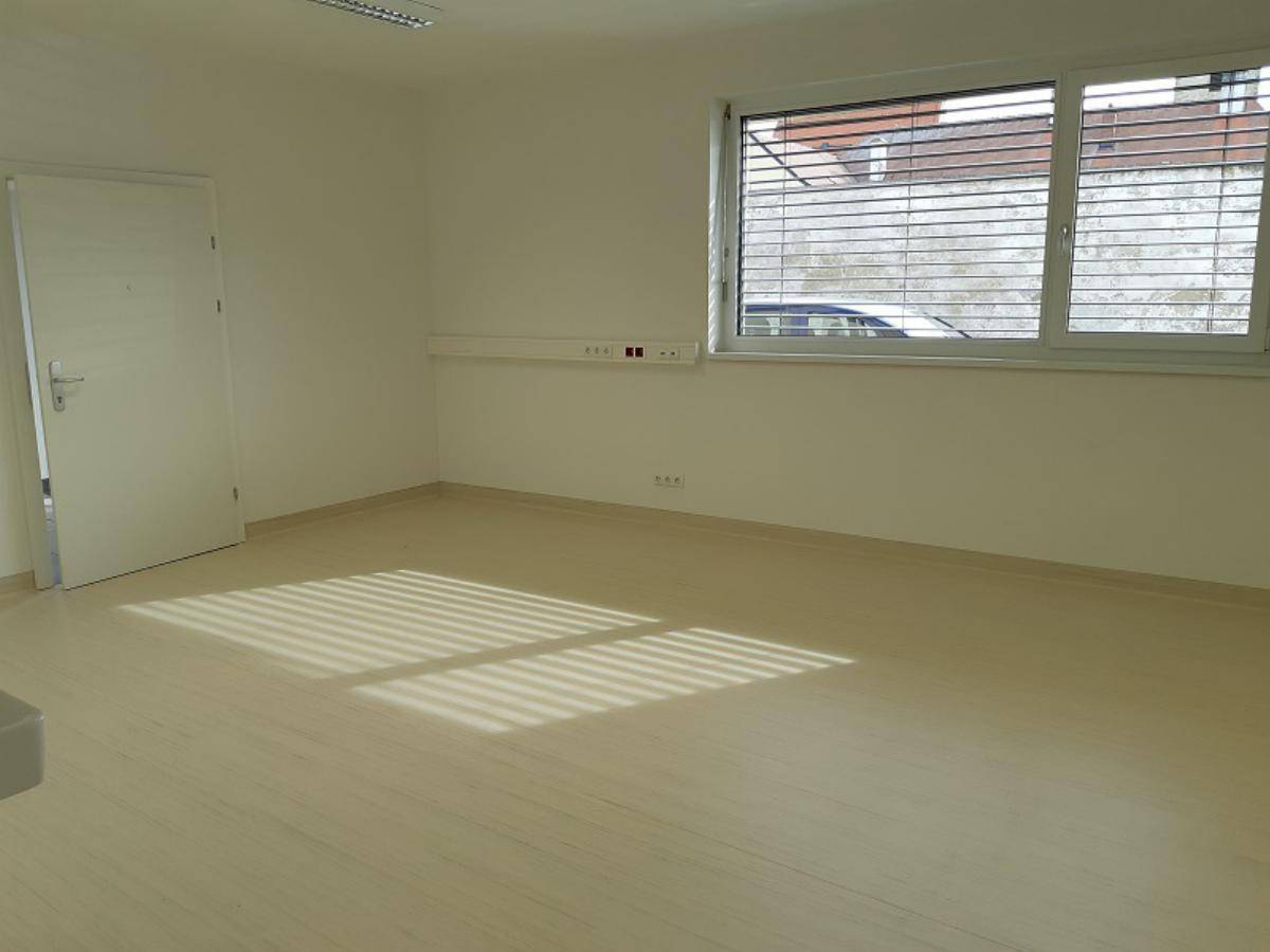Heller Raum mit großem Fenster, hellem Linoleumboden und weißen Wänden, ideal für ein Büro.