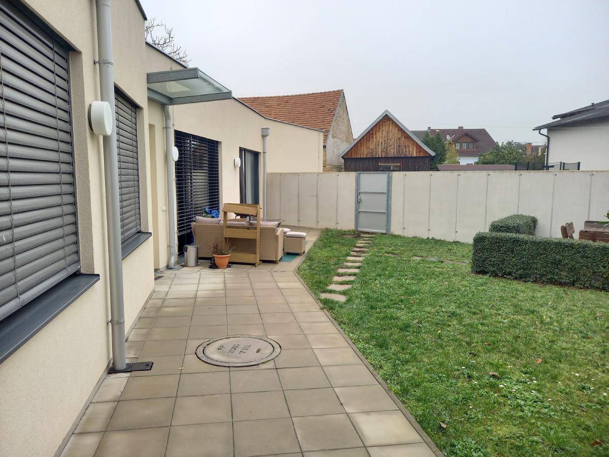 Kleiner Gartenbereich mit gepflasterter Terrasse, Rasenfläche und einer niedrigen Betonmauer.